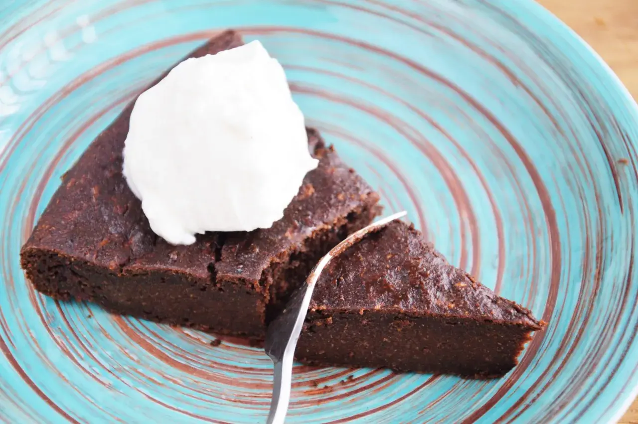 Pyszny brownie z cukinii codziennie fit, podane z bitą śmietaną na turkusowym talerzu.