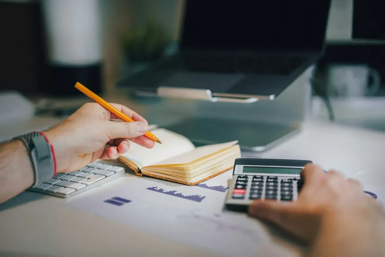 Un avocat postulant analyse des documents financiers avec un crayon, une calculatrice et un ordinateur portable.