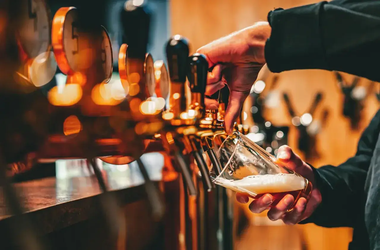 Mano che versa birra da una spillatrice, creando una schiuma perfetta. La spillatura alla tedesca è un'arte.