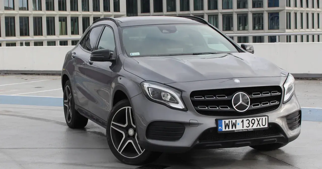 Szary Mercedes GLA 220 z polskimi tablicami rejestracyjnymi stoi na parkingu przed nowoczesnym budynkiem.