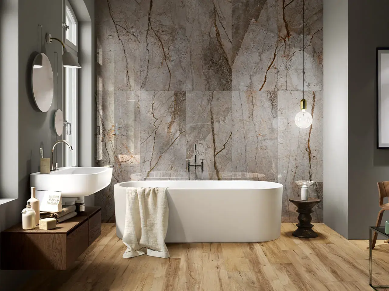 Bagno moderno con vasca freestanding, lavabo sospeso e parete in marmo con venature che si abbinano al legno del pavimento. Idee bagno marmo e legno per un ambiente di lusso.