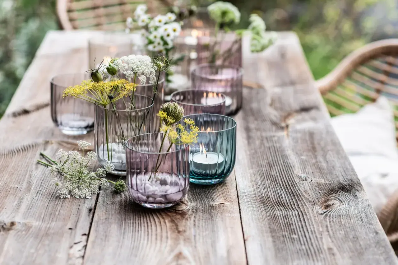 Romantische deko gartentisch mit Blumen und Kerzen in bunten Gläsern.