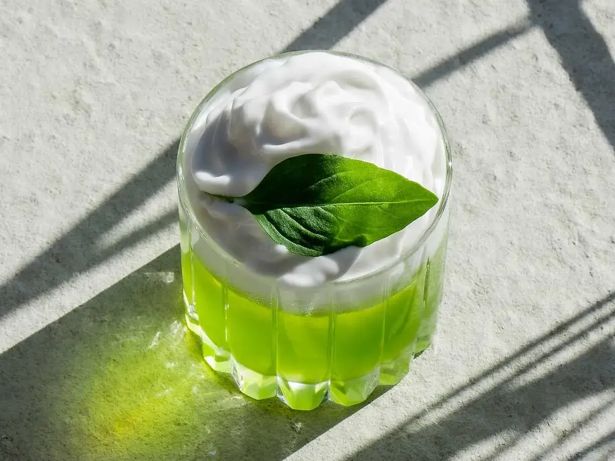 En grön thai basil drink med vitt skum och ett basilika-blad.