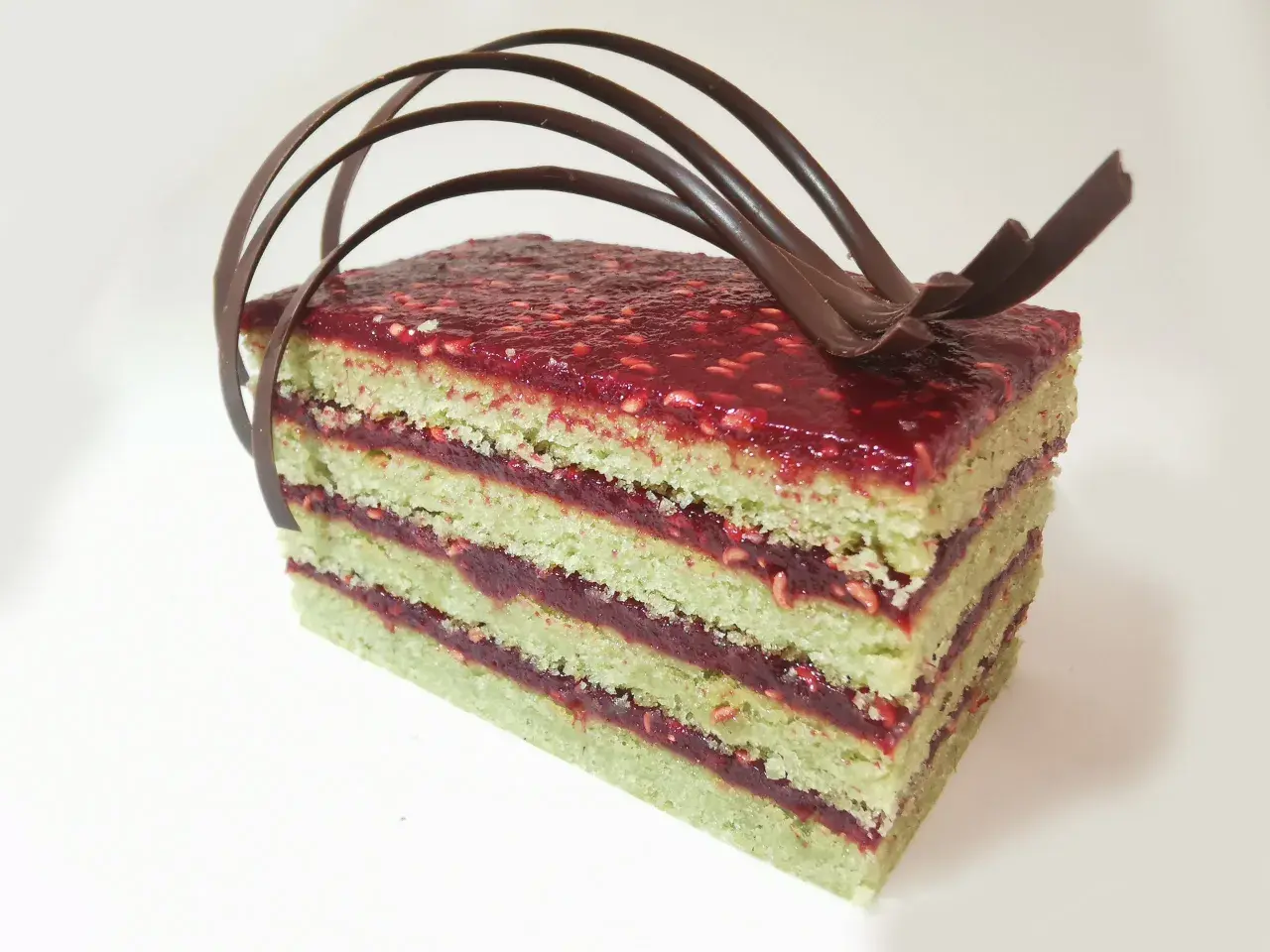 Gâteau pistache framboise mascarpone, une tranche aux couches vertes et rouges, garnie de chocolat.