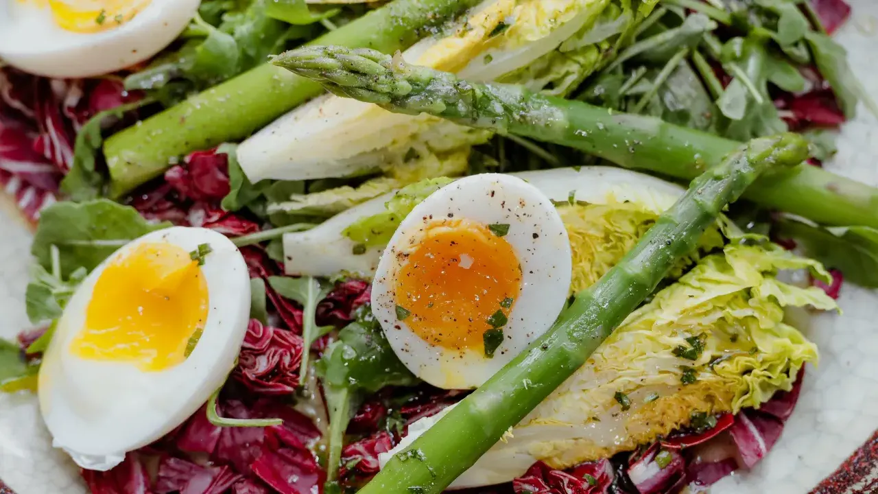 Salade colorée avec des œufs mollets, des asperges vertes croquantes et des feuilles de laitue et de radicchio.