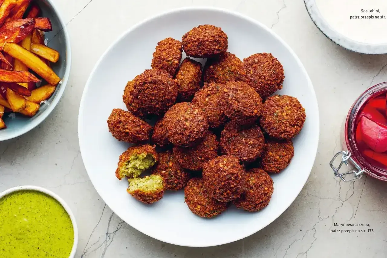 Talerz pełen chrupiących kuleczek, które są odpowiedzią na pytanie: co to jest falafel? Obok sos i frytki.