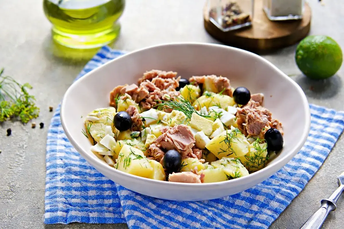 Deliziosa insalata di patate e tonno, arricchita da uova sode, olive nere e aneto fresco. Un piatto gustoso e completo.