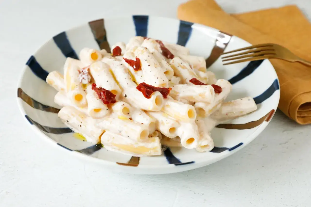 Piatto di pasta cremosa con pesto, pomodori secchi e ricotta. Un gusto mediterraneo in ogni boccone.