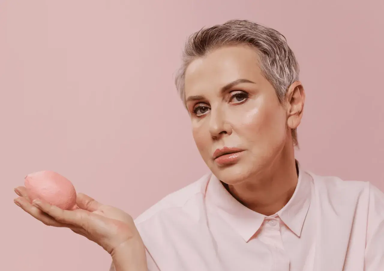 Femme aux cheveux gris et yeux marrons, maquillage subtil, tenant un objet rose.