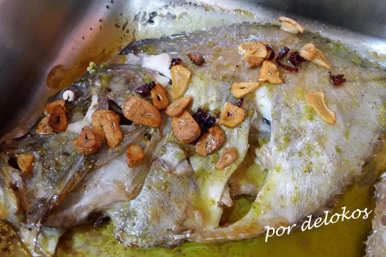 Un delicioso san martiño pescado al horno con ajo laminado y hierbas verdes, bañado en su jugo.