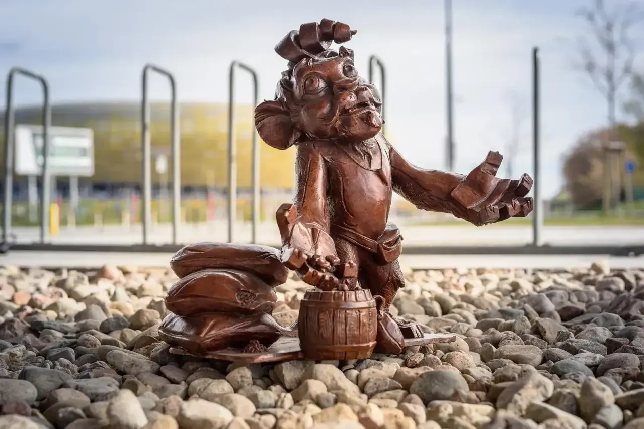 Figurka krasnala z beczką i workami, jeden z lwy gdańskie, stoi na kamieniach przed stadionem.