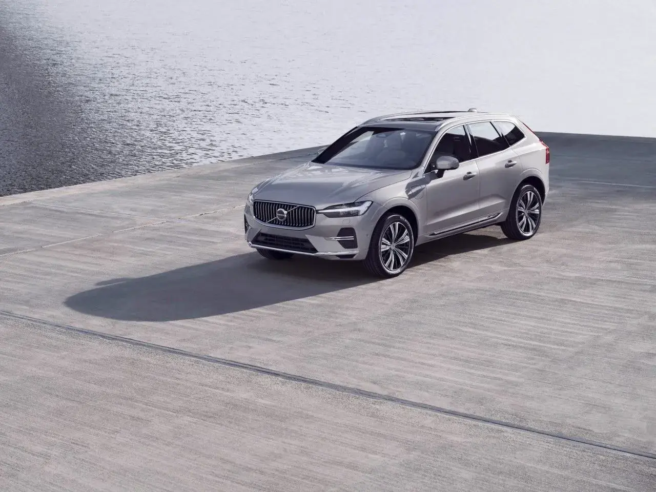 Srebrne Volvo XC60 na betonowym placu przy wodzie. Zwróć uwagę na rozmiar opon, idealnie dopasowany do SUV-a.