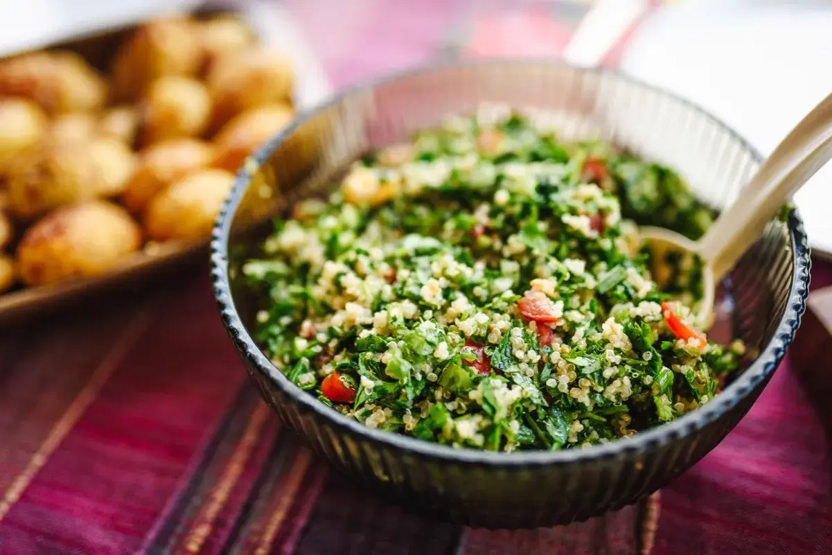 En skål med fräsch tabbouleh, perfekt för ett somrigt tabbouleh recept. Bredvid syns en bricka med små potatisar.