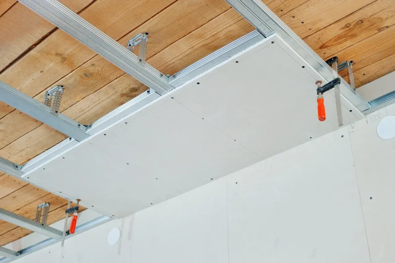 Installation d'un faux plafond en plaques de plâtre pour l'isolation phonique plafond appartement. Structure métallique fixée au plafond bois.