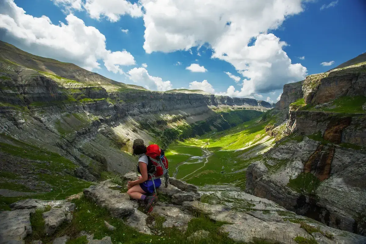 Senderista contempla el impresionante valle de Ordesa en Monte Perdido, Huesca, bajo un cielo azul con nubes algodonosas.