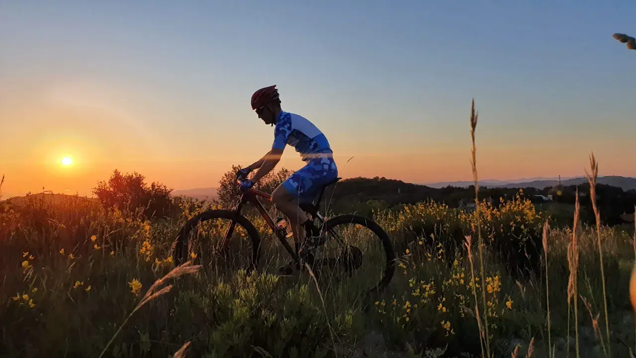 Ciclista in azione al tramonto sul Monte Grimano, tra erba alta e fiori gialli.
