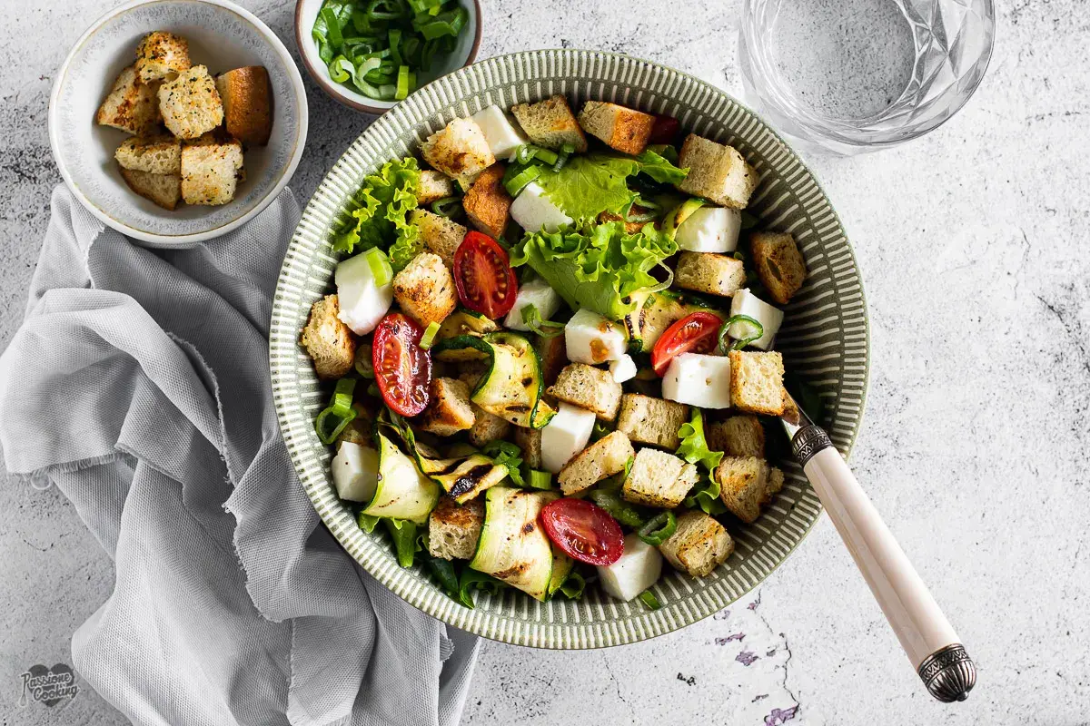 Deliziosa insalata di zucchine grigliate, pomodorini, cubetti di formaggio fresco e crostini croccanti, guarnita con erba cipollina.