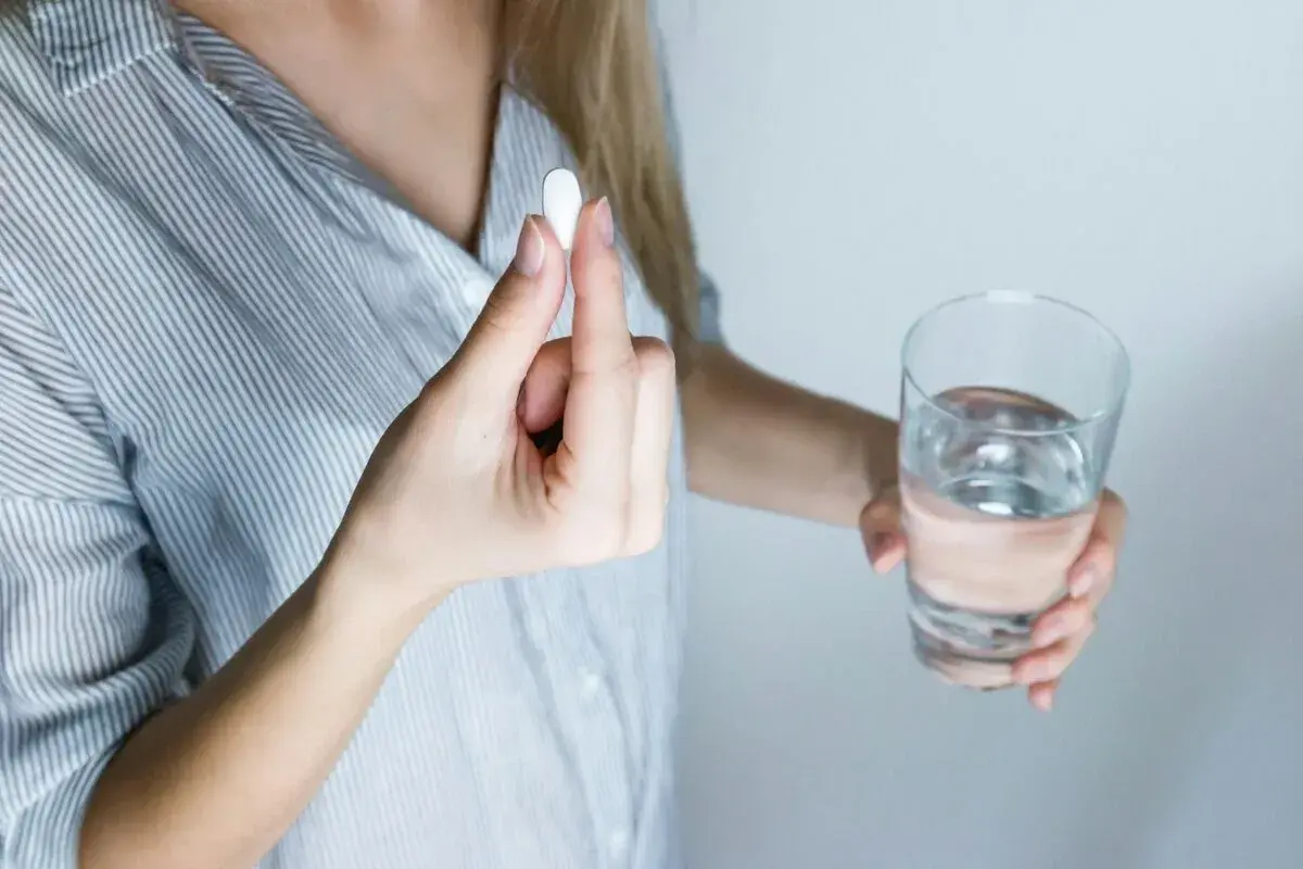 Donna tiene una pillola, forse un antibiotico per denti e gengive, accanto a un bicchiere d'acqua.