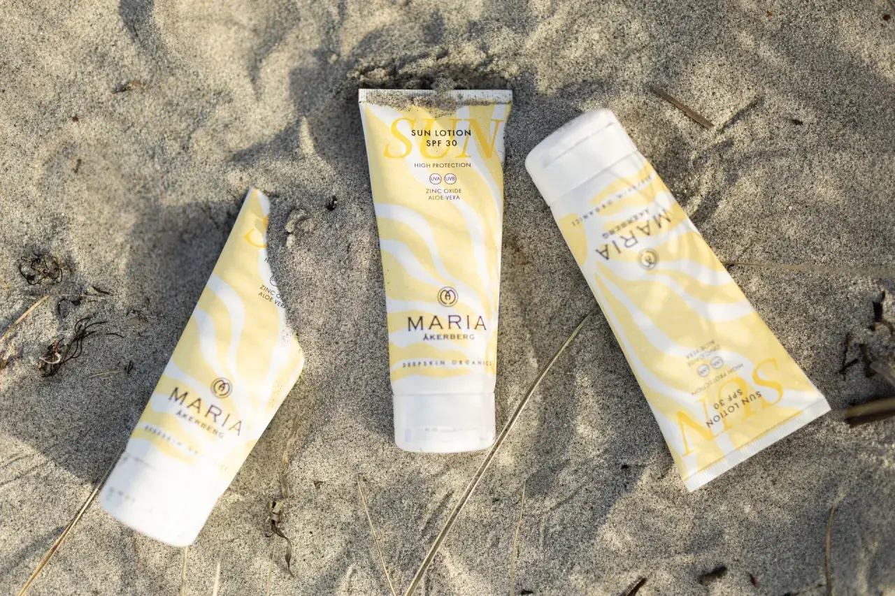 Tre tuber med solskydd från MARIA ÅKERBERG ligger på sanden. Solkrämen har SPF 30 och innehåller zinkoxid samt aloe vera.