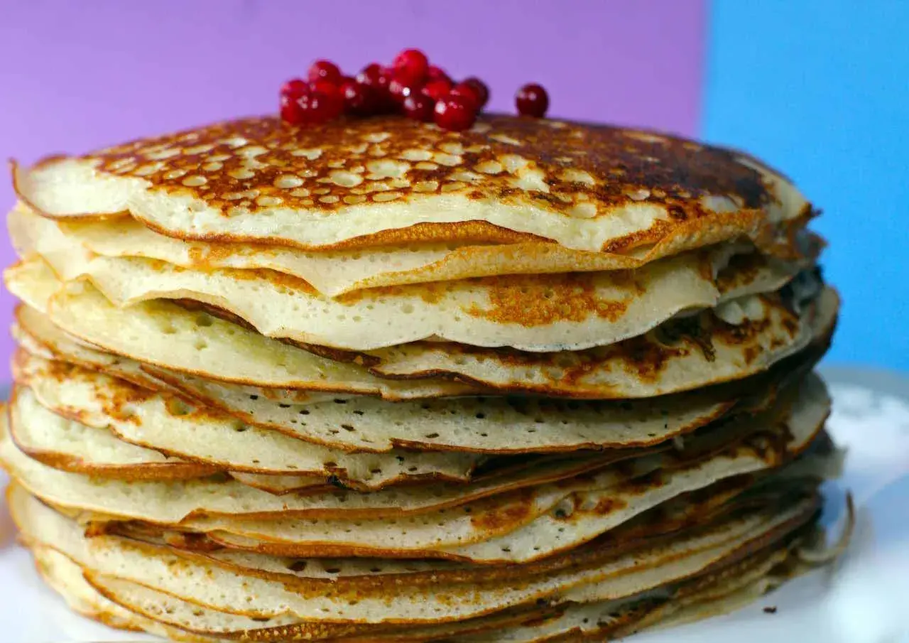 Pila di pancake senza farina, dorati e soffici, guarniti con bacche rosse.