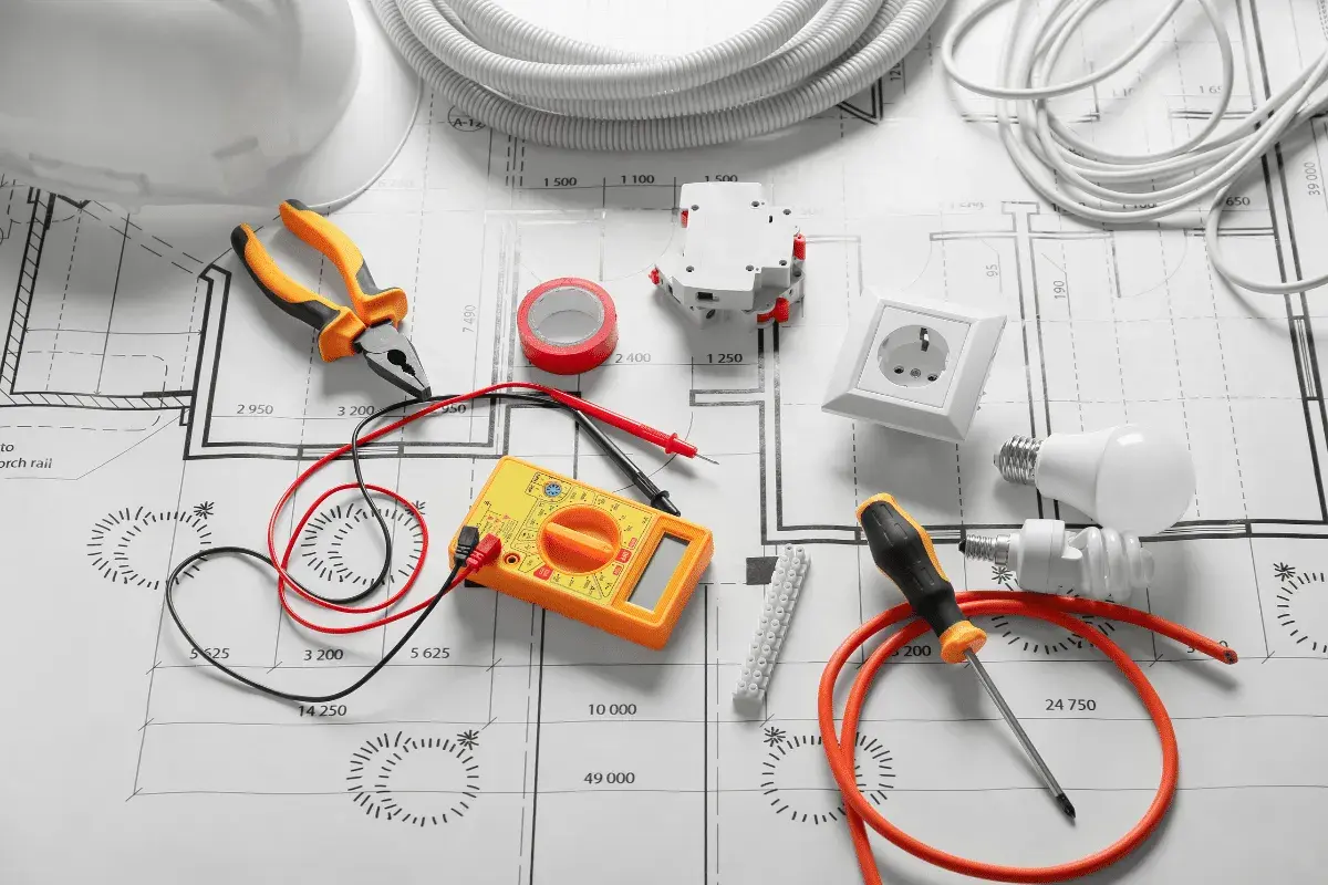 Outils d'électricien et composants sur un plan, pour un devis électricité exemple. Pince, multimètre, prise, ampoules, disjoncteur, ruban adhésif.