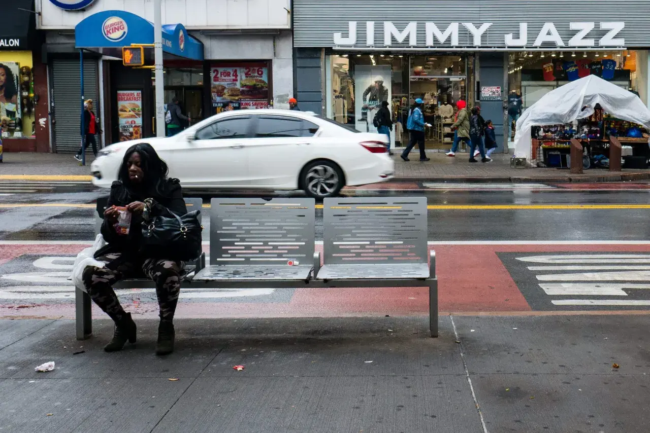 Kobieta siedzi na ławce na ulicy w USA, obok sklepu Jimmy Jazz.