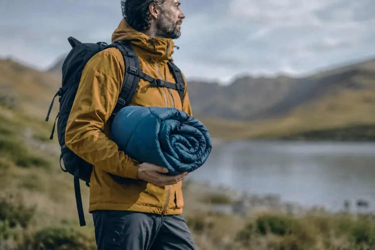 Hombre con mochila y saco de dormir enrollado, listo para elegir su aventura.