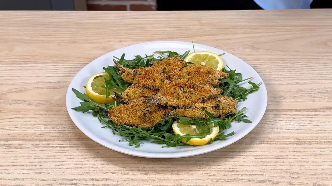 Piatto di alici al forno croccanti, servite su un letto di rucola fresca e guarnite con spicchi di limone.