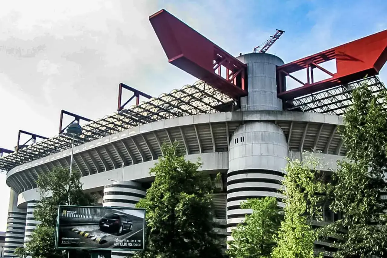 Charakterystyczny stadion Interu Mediolan z czerwonymi elementami konstrukcji i zielenią wokół.