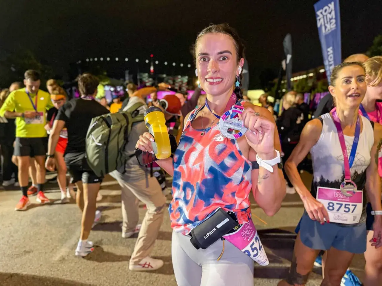 Uśmiechnięta biegaczka po ukończeniu biegu na 100 km, trzymająca medal i bidon.