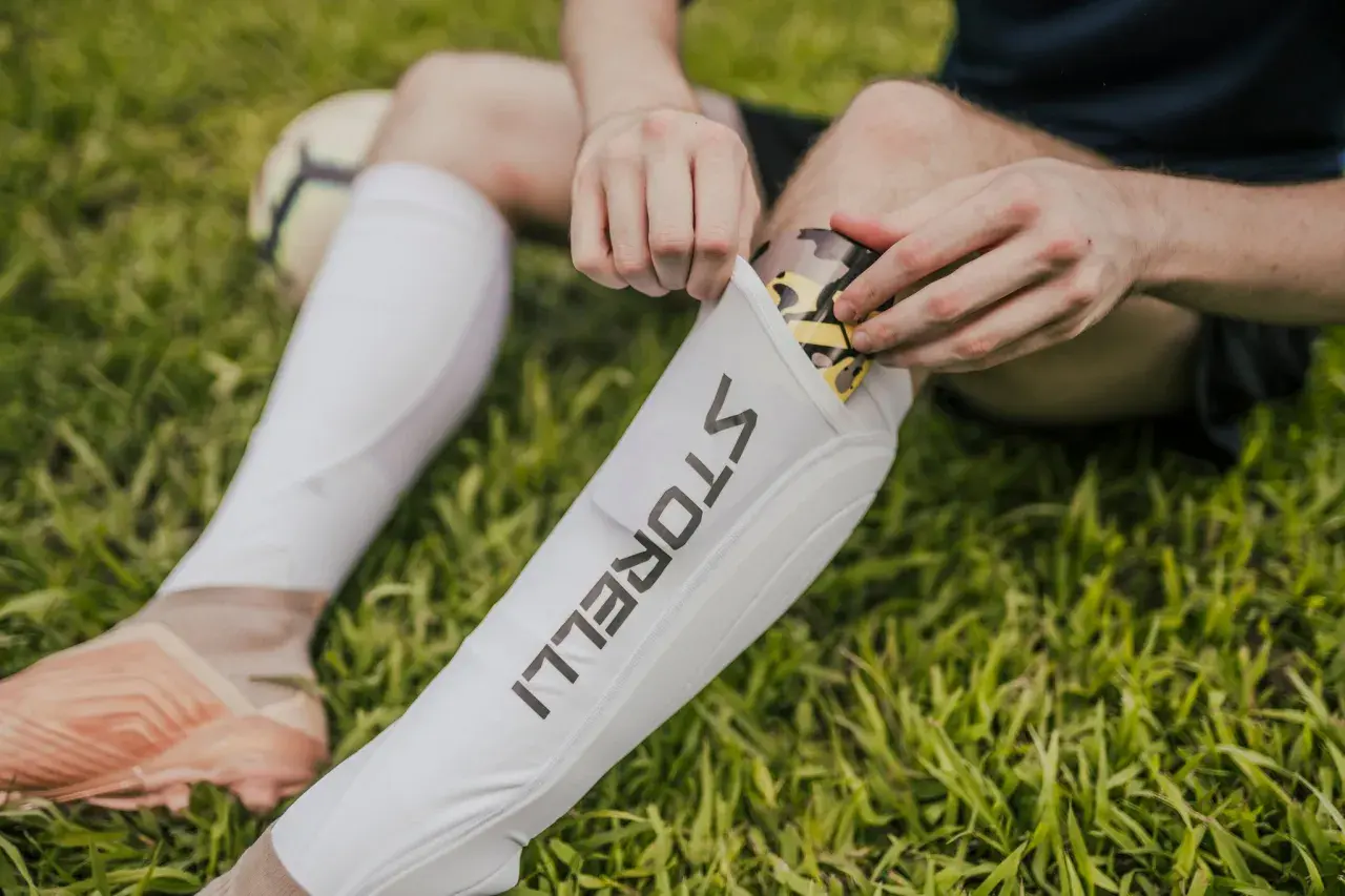 Fußballer legt ein Schienbein Splint mit Tarnmuster in eine weiße Hülle.