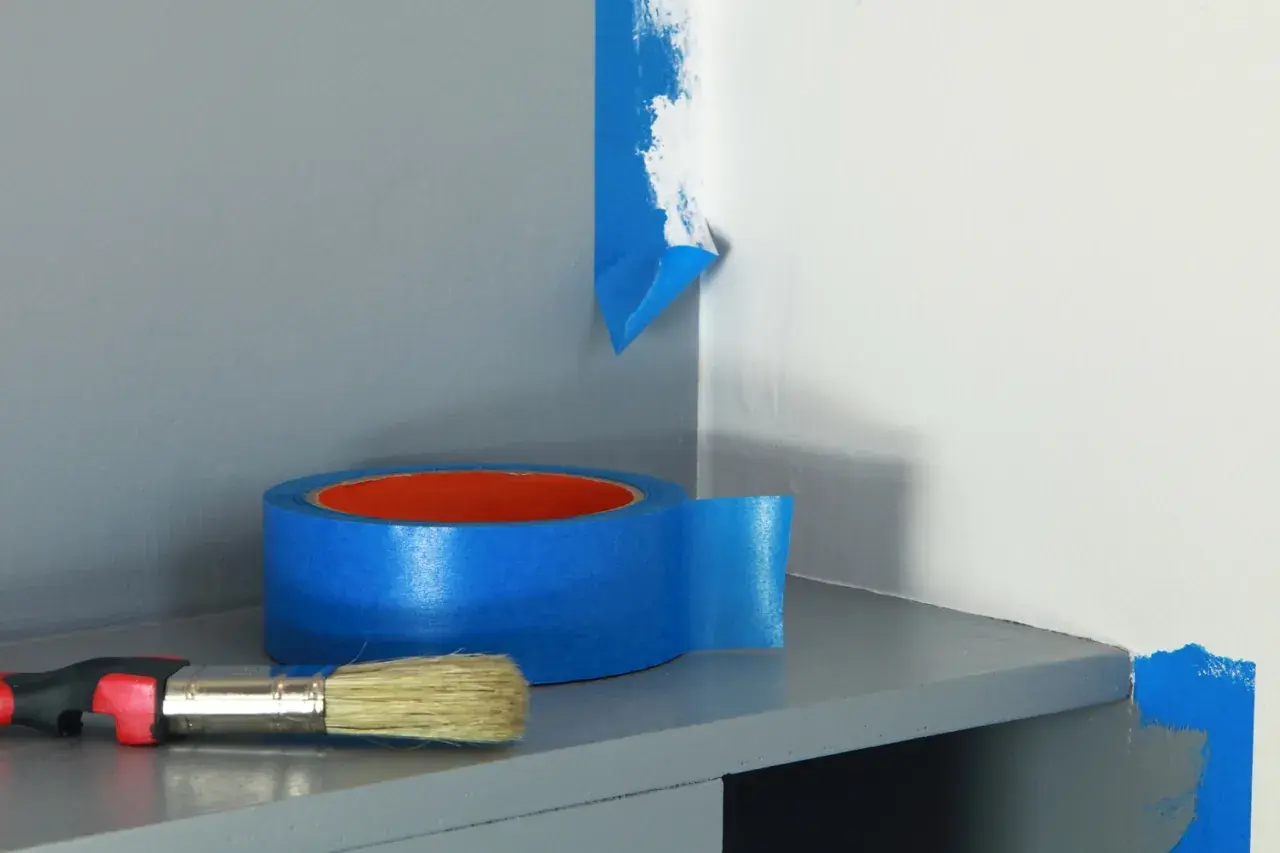 Rouleau de ruban bleu et pinceau prêts à repeindre une partie de mur.