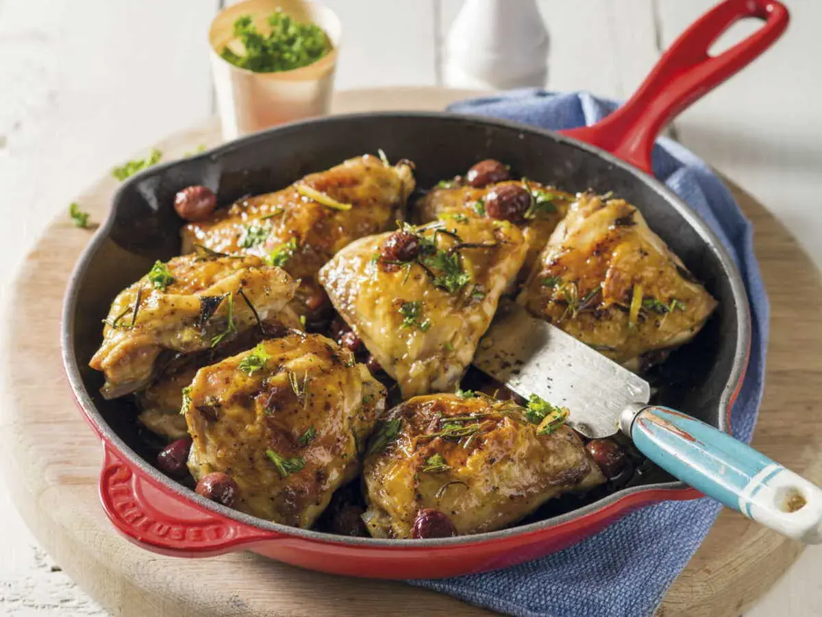 Poêlée de cuisse de poulet dorée, garnie d'herbes et de quelques baies rouges, prête à être servie.