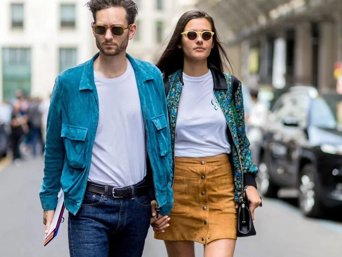 Ein Paar geht Hand in Hand, bereit für ein erstes Date. Er trägt eine blaue Jacke, sie einen gemusterten Blazer.