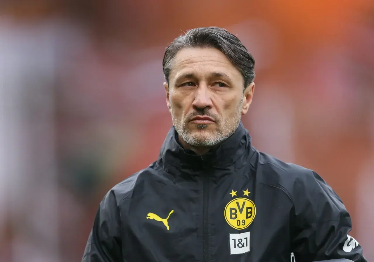 Kovac trener w czarnej kurtce z logo BVB, skupiony na boisku.