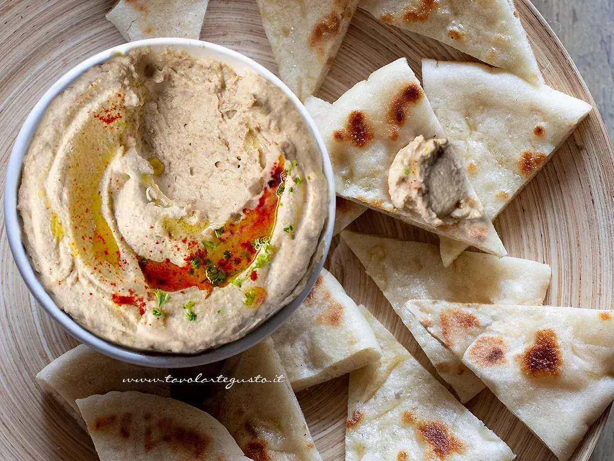Ciotola di hummus di lenticchie con olio, paprika e prezzemolo, servito con pane pita tagliato a spicchi.