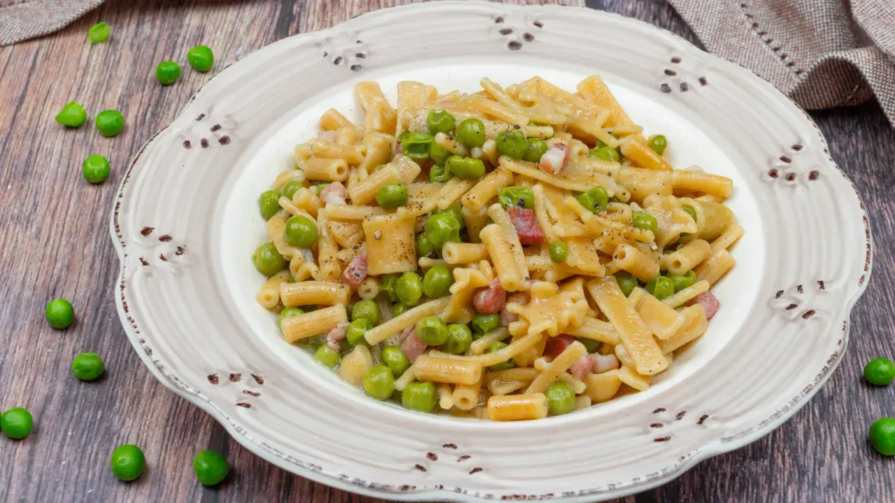 Un piatto di pasta con piselli, pancetta e pepe nero, servito su un piatto rustico.