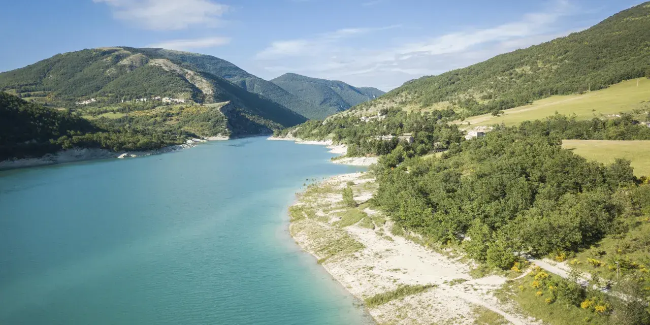 Spiaggia libera sul lago di Fiastra, con acque turchesi e montagne verdi sullo sfondo. Un luogo ideale per rilassarsi e godersi la natura.