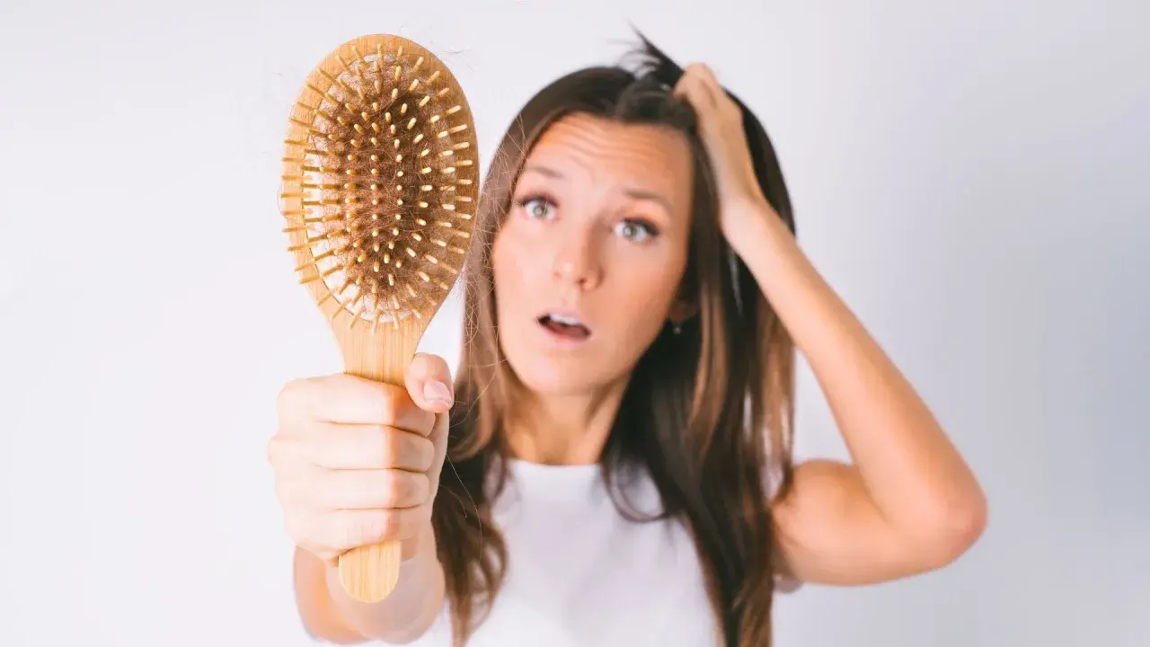 Mujer preocupada por la caída de pelo postparto, mostrando un cepillo con cabello.