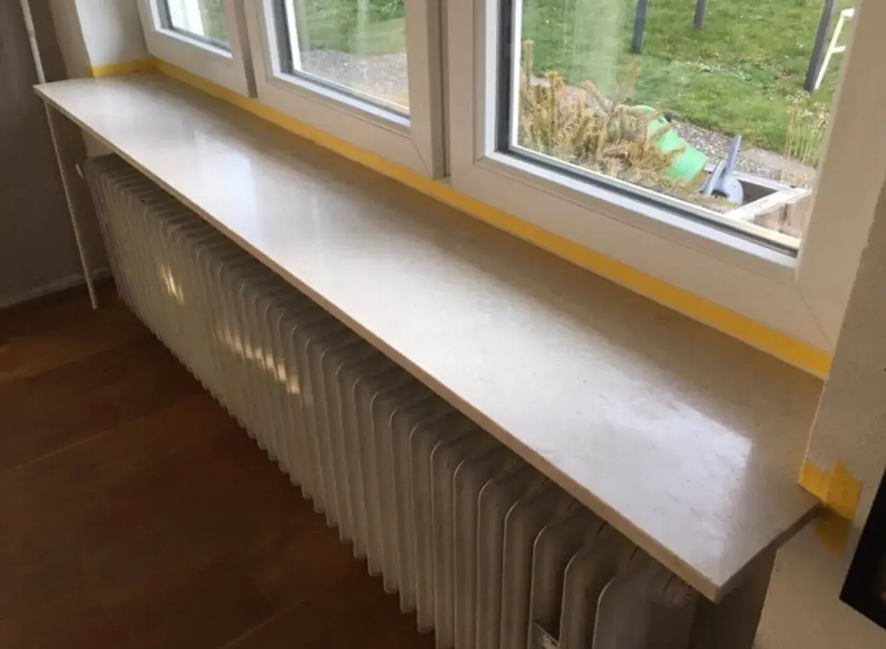 Un nouveau rebord de fenêtre en pierre, prêt à accueillir des plantes, surplombe un radiateur blanc.