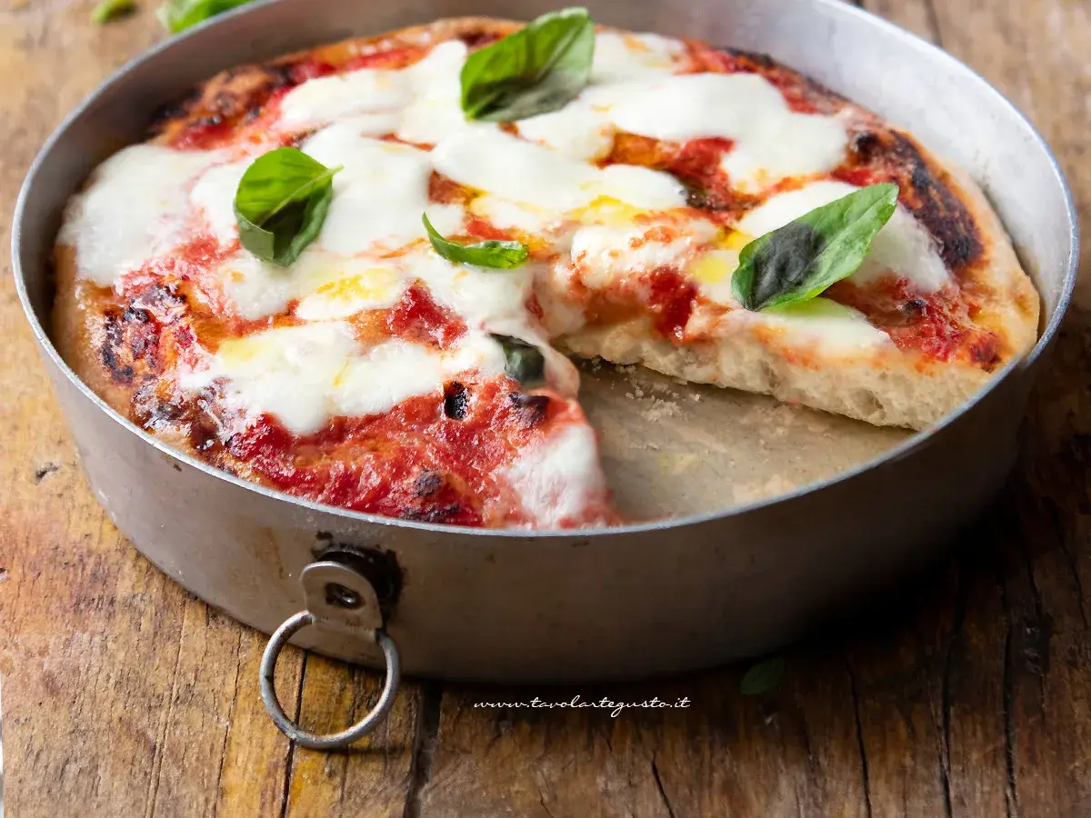 Pizza margherita appena sfornata in friggitrice ad aria, con mozzarella filante e basilico fresco su un tagliere di legno.