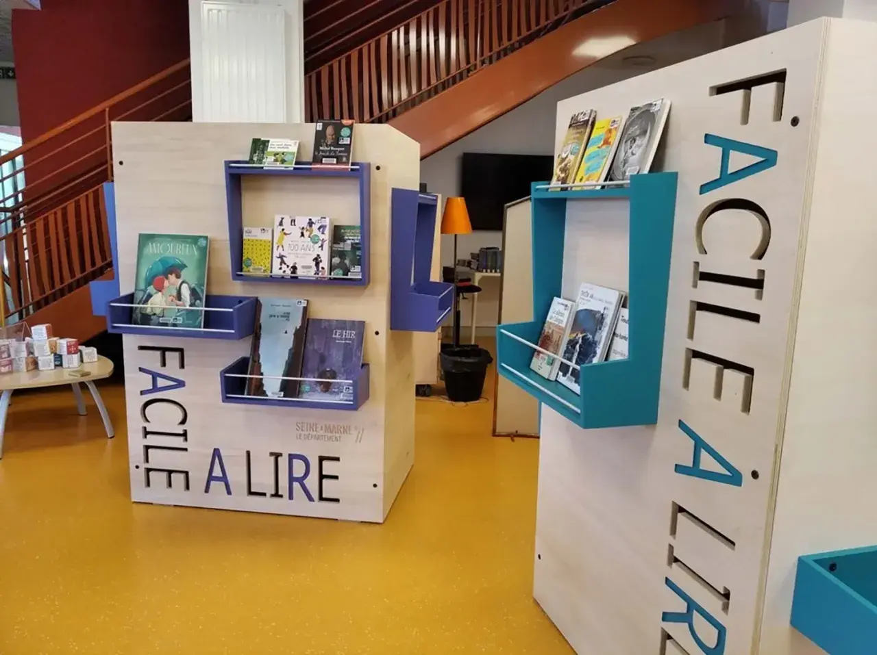 Étagères de livres bleues et turquoises sur des présentoirs en bois avec l'inscription "FACILE À LIRE". Un barrage défensif de livres pour tous.