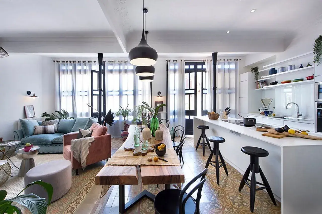 Un salón-comedor moderno con sofás azules y rosas, una mesa de madera rústica y **lámparas grises de techo** colgantes sobre la mesa.