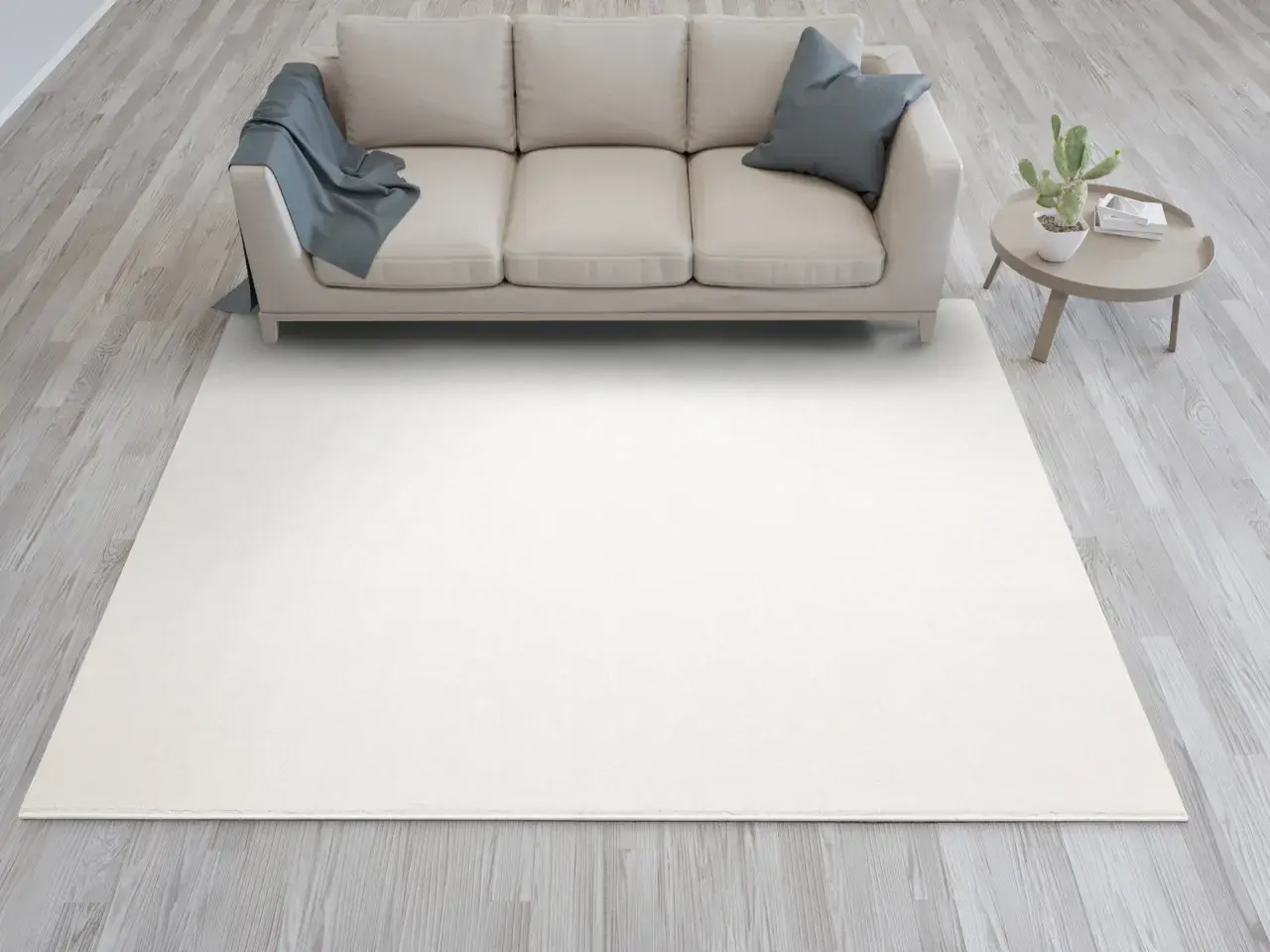 Jasna sofa w kolorze kość słoniowa, z niebieskim kocem i poduszką, stoi na jasnym dywanie. Obok stolik z kaktusem.