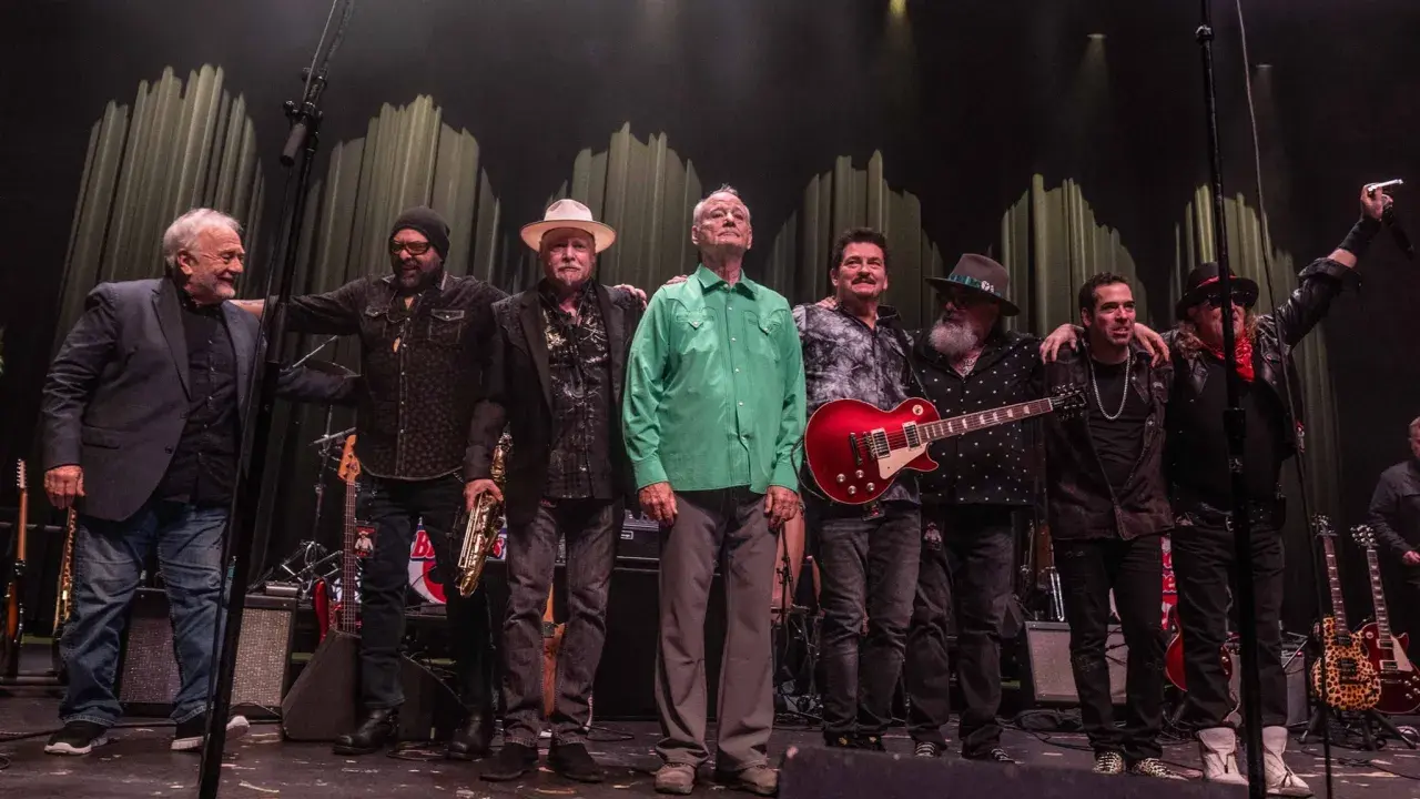 Zespół muzyczny na scenie, w tym Bill Murray w zielonej koszuli, gotowy na koncerty.
