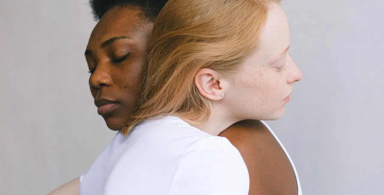 Twee vrouwen, één met donkere huid, de ander met lichte huid, omhelzen elkaar. Een beeld van verbinding, dat het verschil tussen compassie en empathie illustreert.