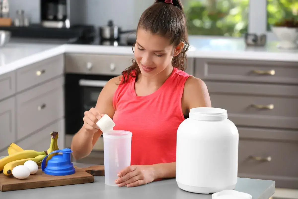 Donna prepara un frullato con proteine prima o dopo allenamento, con banane e uova sul bancone.