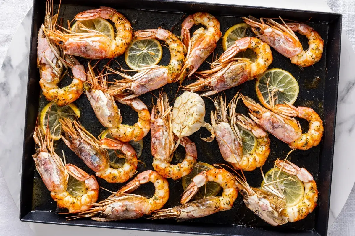 Gamberoni al forno dorati e succulenti, conditi con erbe aromatiche e fette di limone, pronti per essere gustati.