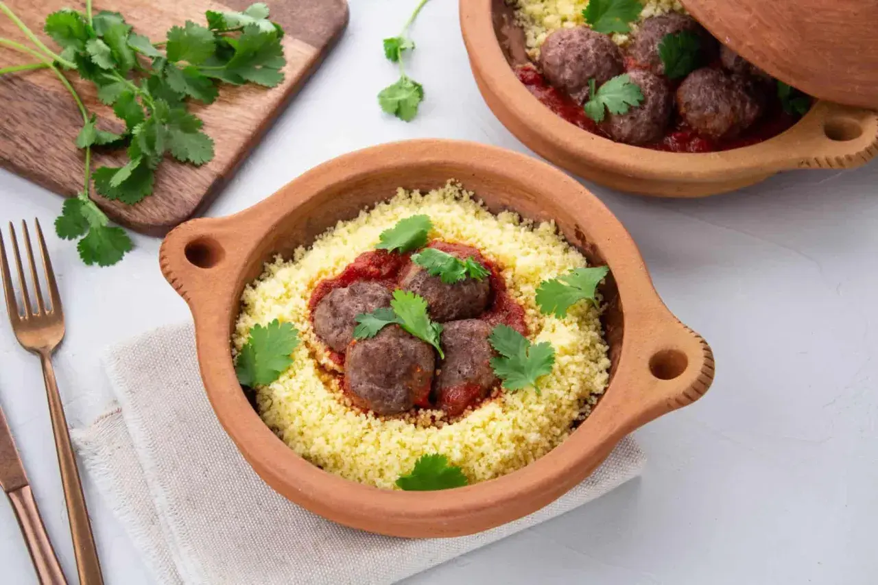 Délicieuse recette de boulette de boeuf haché avec sauce, servie sur un lit de couscous et garnie de coriandre fraîche.