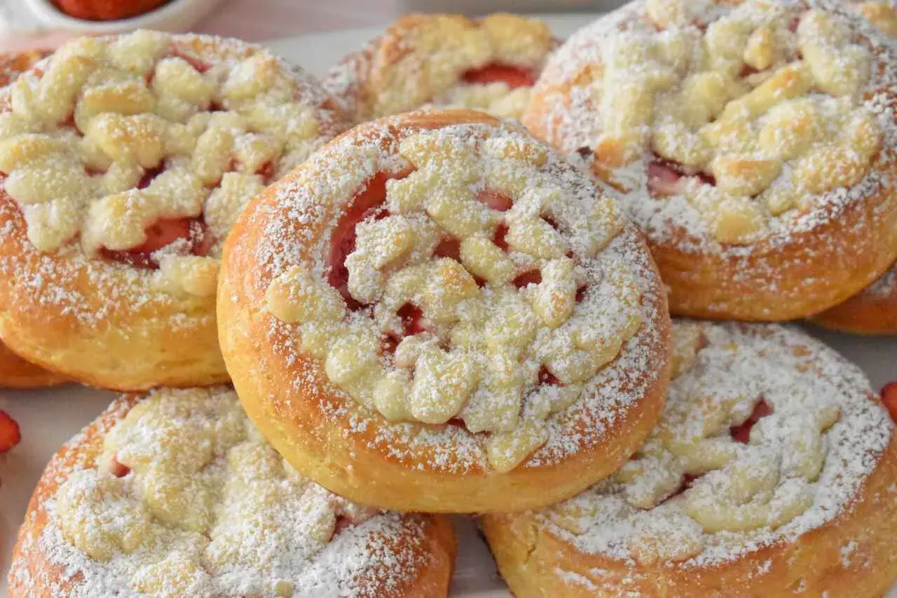 Puszyste drożdżówki z truskawkami, posypane cukrem pudrem i kruszonką. Idealne na letnie popołudnie.